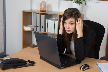 累了的业务女人坐在桌前，在灰色的背景。在笔记本电脑上看