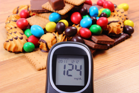 血糖仪与堆的甜食对木质的表面 糖尿病和不健康的食物