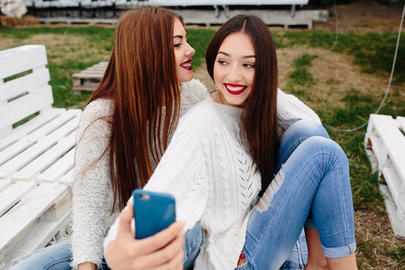 两个女孩坐在板凳上使自拍照