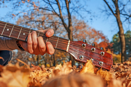 男人在秋天公园的抱着吉他脖子附近