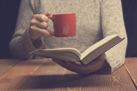 读一本书，拿着杯茶或咖啡的年轻女人。色调的图像