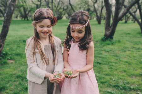 在春天的花园里摘花的两个快乐小女友。姐妹花时间在一起户外。季节性的活动