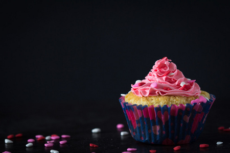 单杯形蛋糕和粉红色散洒在深色背景上的糖霜