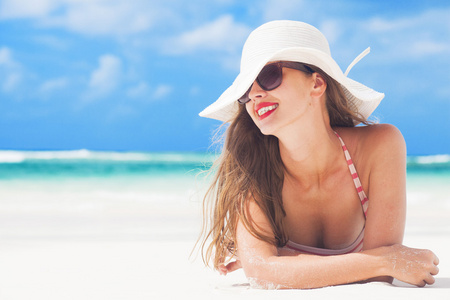年轻女子在一顶帽子在地处热带的海滩和条纹游泳衣