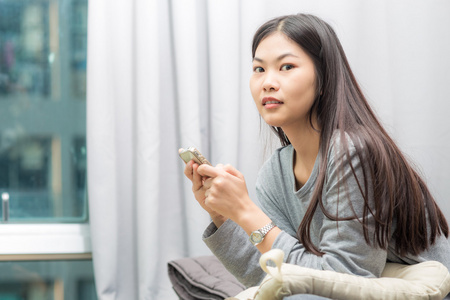 放松的亚洲女人在家在现代卧室里用手机