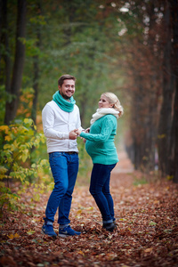 怀孕的女人和一个男人走在秋天的公园