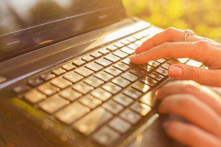 在阳光明媚的户外，女人在笔记本电脑键盘上打字。