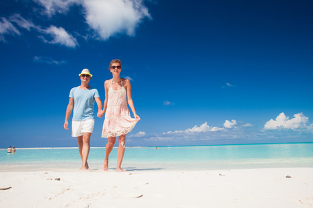在明亮的衣服和帽子在热带海滩玩夫妇