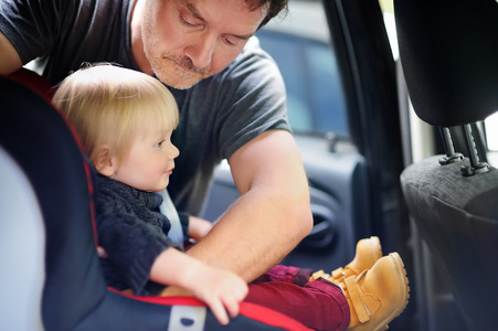 父亲帮助他的儿子在汽车座椅上的安全带