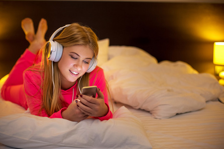 从智能手机在床上听音乐的年轻妇女