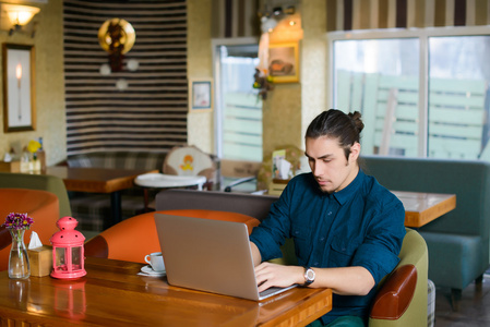 年轻人喝着咖啡，在一家咖啡馆的笔记本电脑上工作