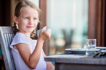 可爱的小女孩在户外咖啡馆吃早餐与茶