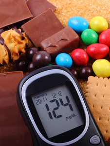 血糖仪与堆的糖果和褐色蔗糖 不健康的食物