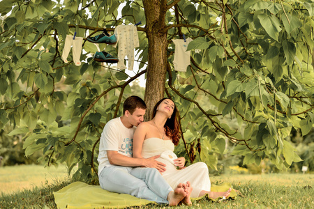 快乐怀孕的夫妻坐在公园里下属