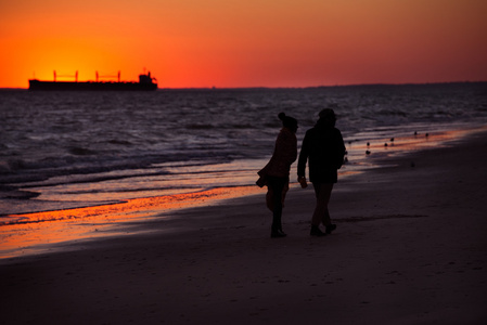 日落时分，一对夫妇在海边散步的剪影