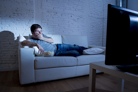 有魅力的男人躺在客厅的沙发上看电视