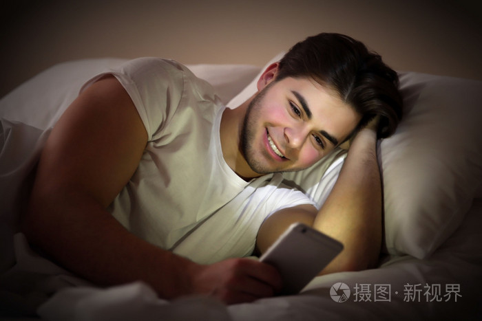 躺在床上用手机在卧室里的年轻人