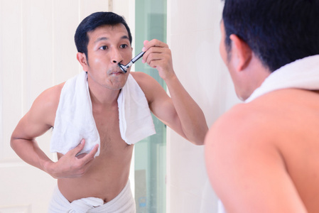 年轻英俊的男人用镜像由自己剃须