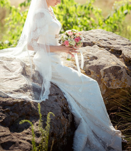 坐在岩石上的花束的新娘