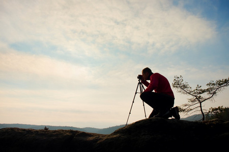 业余摄影师带镜相机的岩峰上的照片。梦幻般顽固景观 春橙色粉红色雾日出