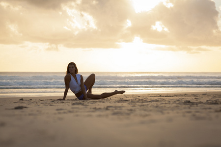 合适的女人在日出时在海滩上伸展