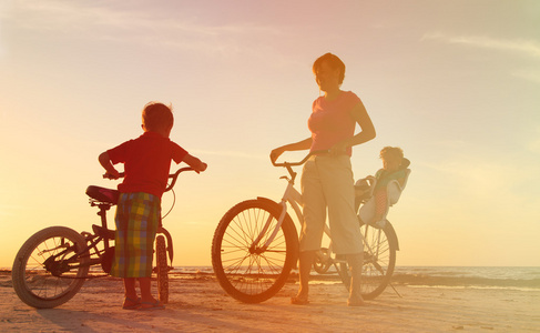 快乐的妈妈，有两个孩子骑自行车在日落时分