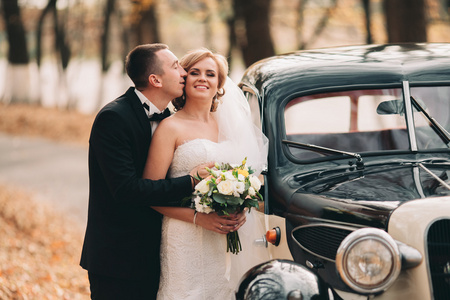 时尚的婚礼夫妇，新娘，新郎亲吻和拥抱附近复古车在秋天