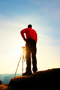 专业摄影师的照片带在岩石峰上三脚架上的相机。梦幻般的春景