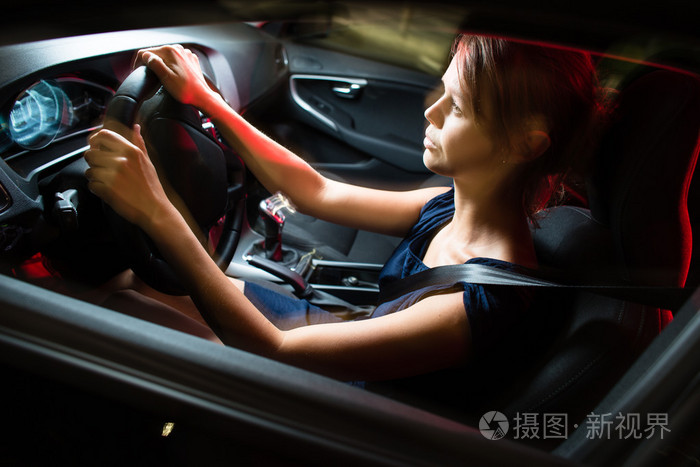 一辆汽车在夜间开车-漂亮,年轻女人驾驶她的车