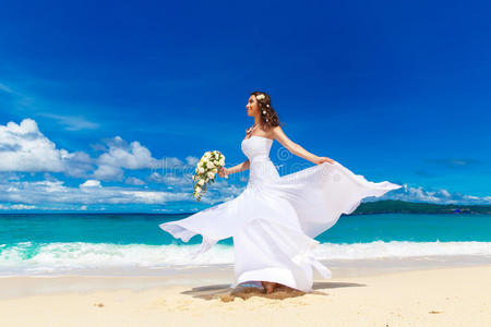 美丽的黑发新娘穿着白色婚纱，白色的大火车和婚礼花束站在海边。 热带地区