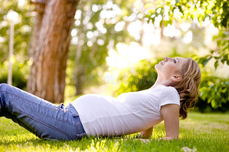 阳光明媚的日子里，美丽的孕妇躺在草地上。 抬头看