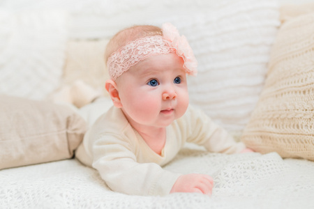 胖胖的脸颊与花与针织枕头躺在床上穿着白色的衣服和粉红色带惊讶可爱的小宝宝。婴儿期和童年的概念