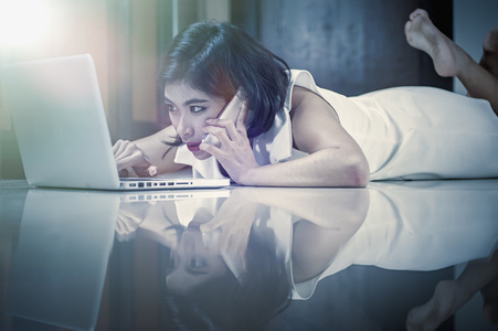 亚洲女人使用智能手机和笔记本电脑躺在地板上