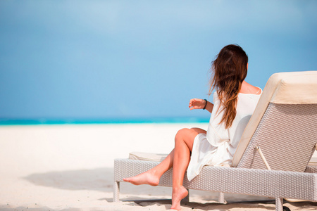 年轻的女子在与手机在沙滩的躺椅