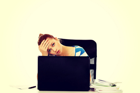 疲惫的青少年女子，坐在桌子后面的笔记本电脑