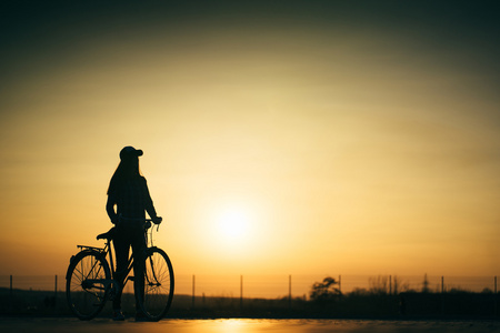 用一辆自行车在日落路上美丽时髦女孩
