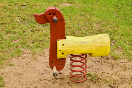 儿童五颜六色的木制摇摆狗在操场上。木跷跷板
