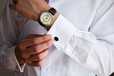 男性手上一件白色的衬衣，长袖衬衫袖扣和手表，背景拍摄特写
