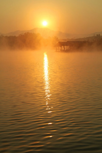 与木房子在湄 Ngad 水坝和水库，泰国清迈，湖面上薄雾热带日落