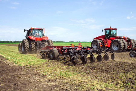 现代科技红色拖拉机犁地绿色农业在春天在农场上。播种小麦收割机