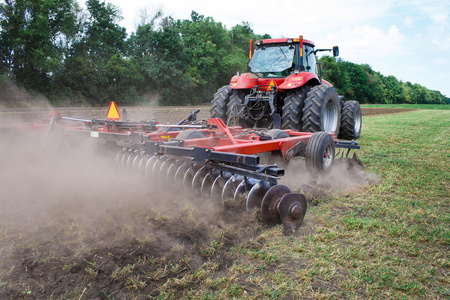 现代科技红色拖拉机犁地绿色农业在春天在农场上。播种小麦收割机