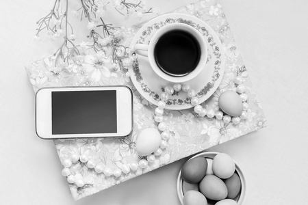电话与一杯茶和花缎白色背景上的珍珠项链。书 茶杯 电话和装饰。下午茶时间和复活节彩绘鸡蛋