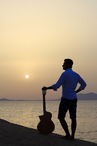 看着早晨的阳光下的海滩上的吉他手