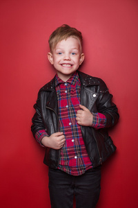 时尚小男孩穿着一件皮夹克。在红色背景的工作室画像
