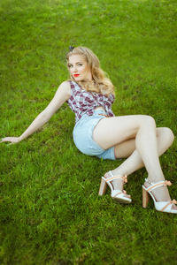 金发女孩穿着短裤坐在室外的草地上
