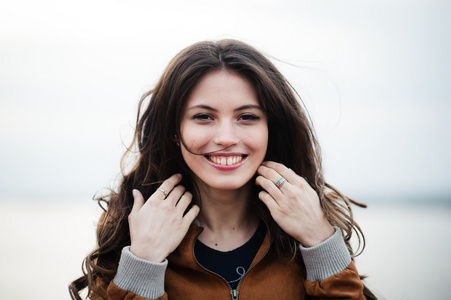 年轻快乐美丽漂亮的女性穿着皮革外套微笑着站在户外光线背景的特写肖像
