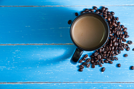 蓝色木制背景上有咖啡豆的咖啡杯。