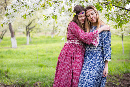 长裙子母亲和女儿两个漂亮女人走在郁郁葱葱的春天的花园