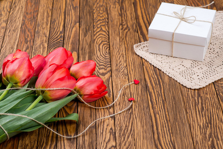 红色郁金香花束和一个礼品盒，木制的桌子上
