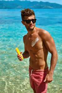 性感男人用防晒霜在身体皮肤上晒黑。 夏季